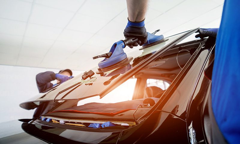 Automobile special workers replacing windscreen or windshield of a car in auto service station garage. Background